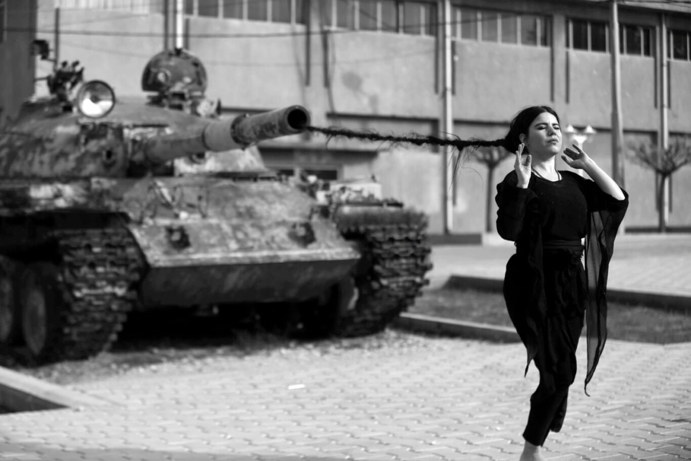 Artist Zehra Doğan performance, walking in front of a tank with her long hair coming out of the tank's cannon.