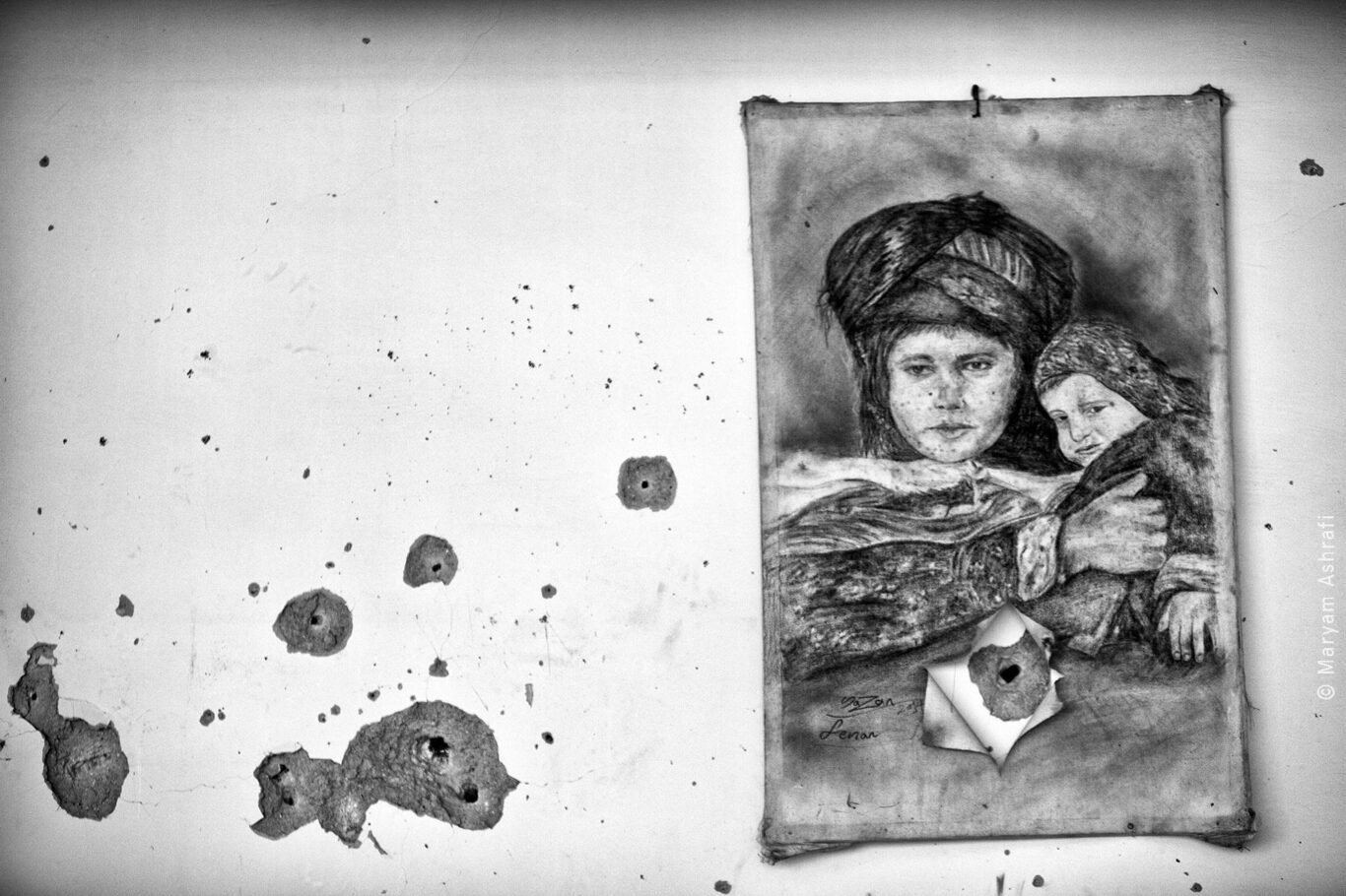 Painting of a mother holding her child hung on a wall damaged by bullets.