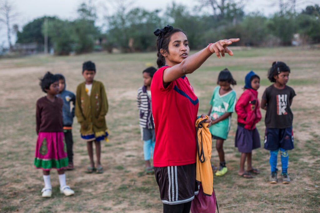 A woman football coach is instructing boys and girls to play football in Jharkhand, India.