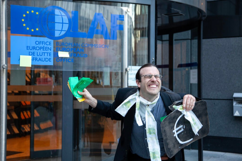 A protester throwing fake money in front of European Anti-Fraud Office whose name is defaced as "Fraud Office".