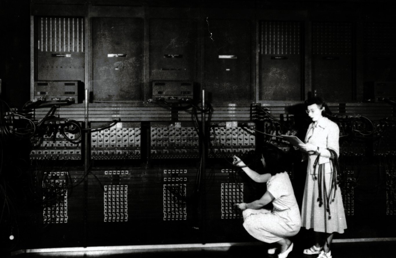 Programmers Ruth Lichterman (crouching) and Marlyn Wescoff (standing) wiring the right side of the ENIAC with a new program.