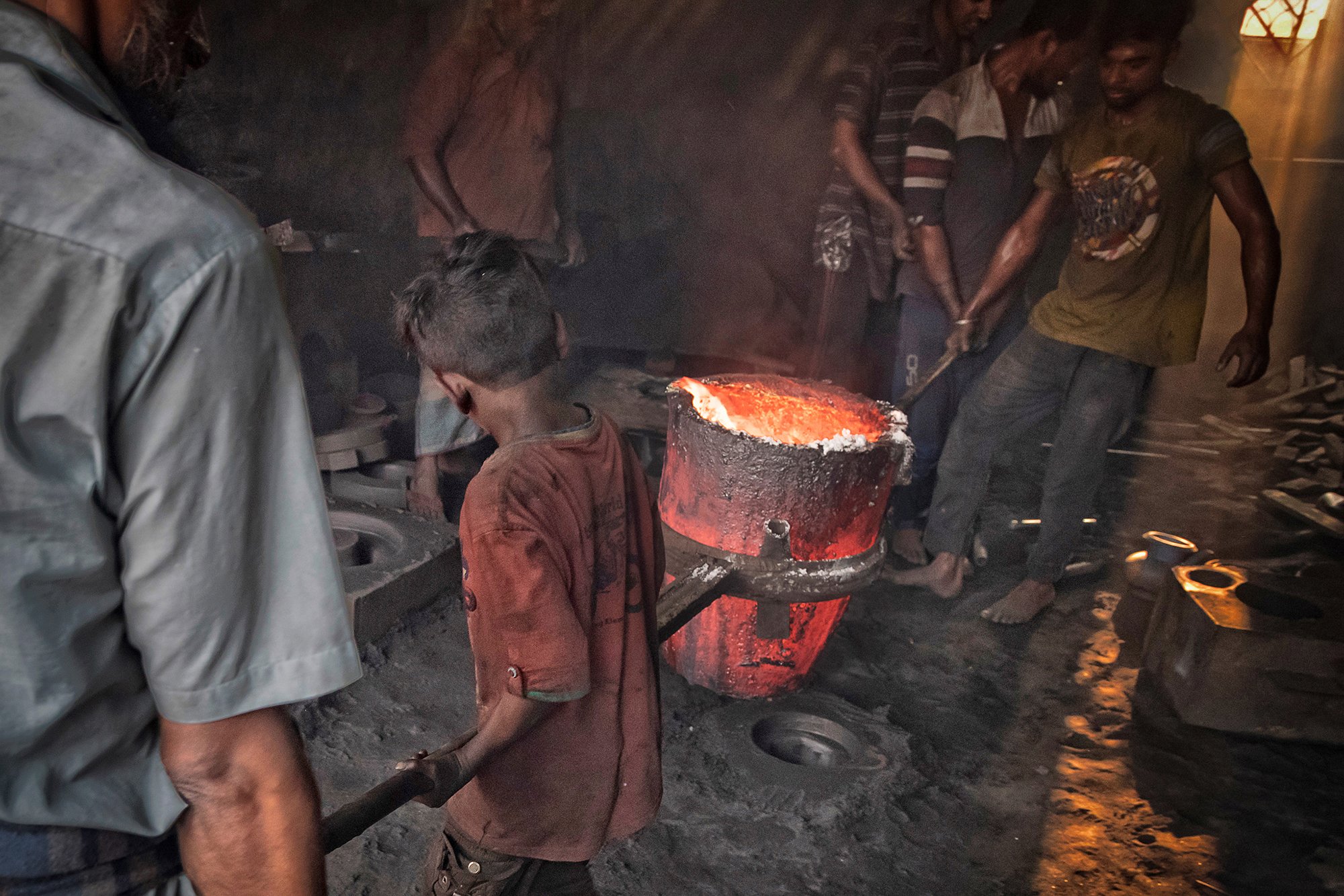 A chilld and few adults melt metal in hazardous working conditions in Dhaka, Bangladesh.
