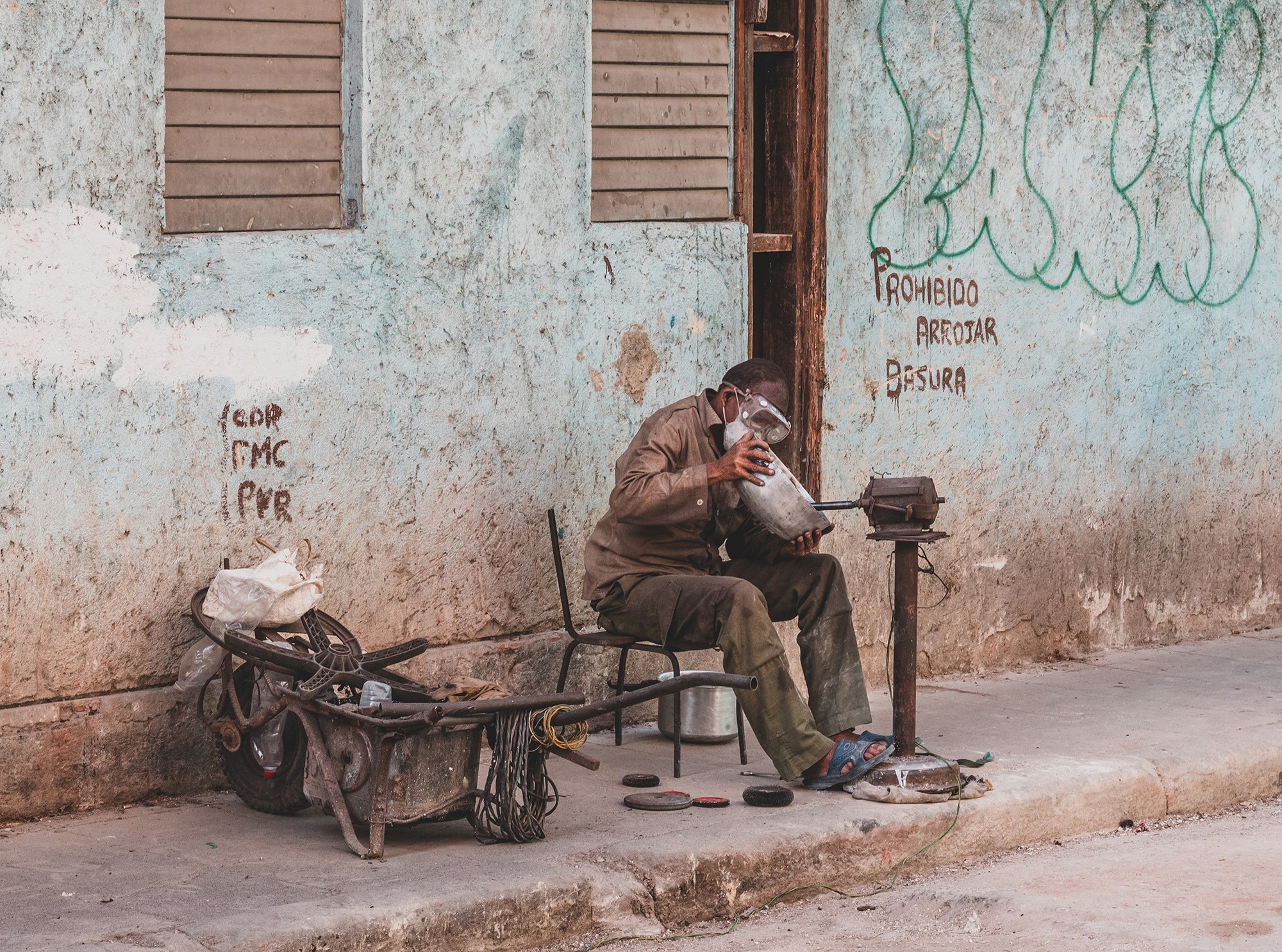 A worker in Havana has a covid-19 mask while tending a pot with his small machine on the street.