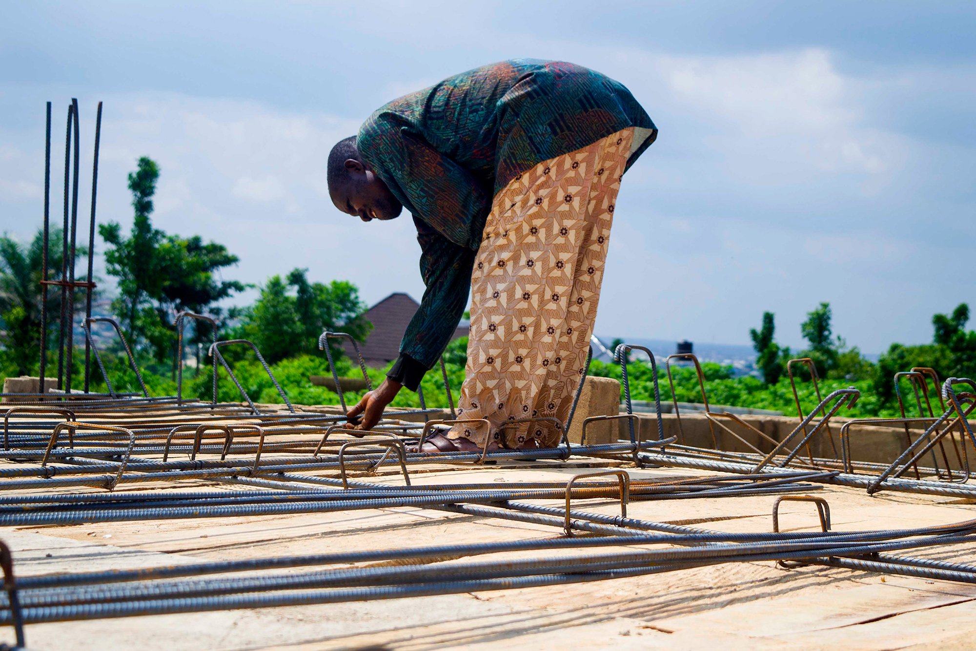 An irregular and self-employed Nigerian worker inspects steel rods and cement in Ibadan.