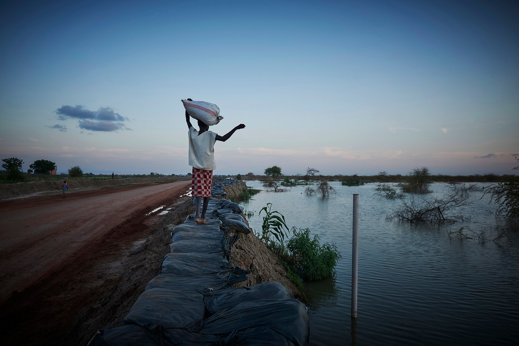 A young girl walks along the apex of a dyke separating the flooding from the roads in Bentiu surroundings. ⁠