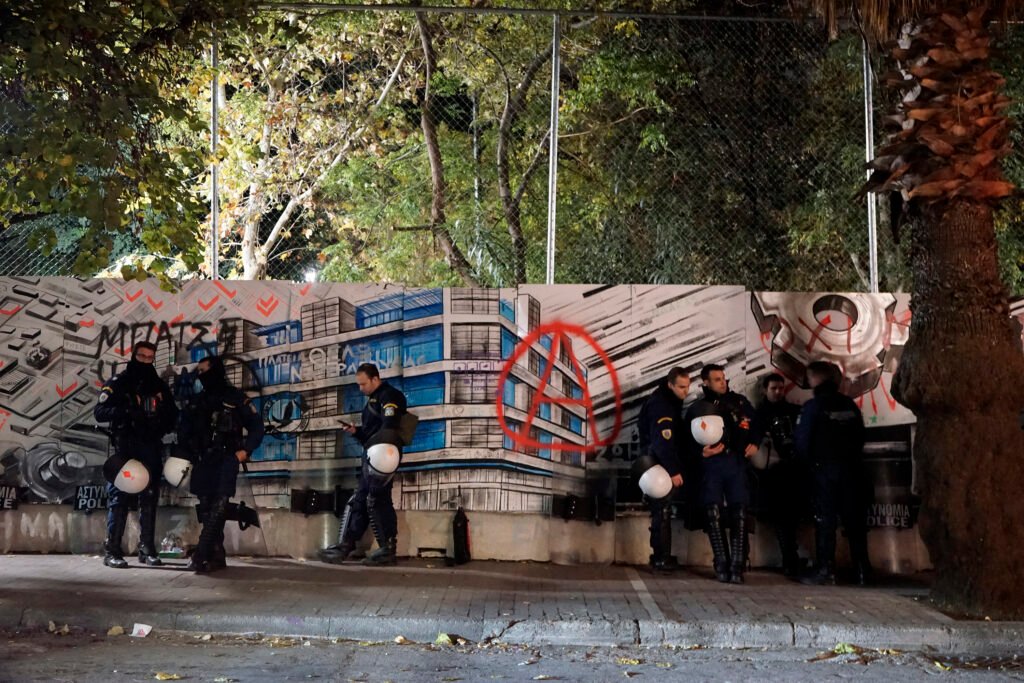 Police officers rest around anarchist graffiti on the 5 meter high fence separating Exarchia square from the neighbourghood in Athens.