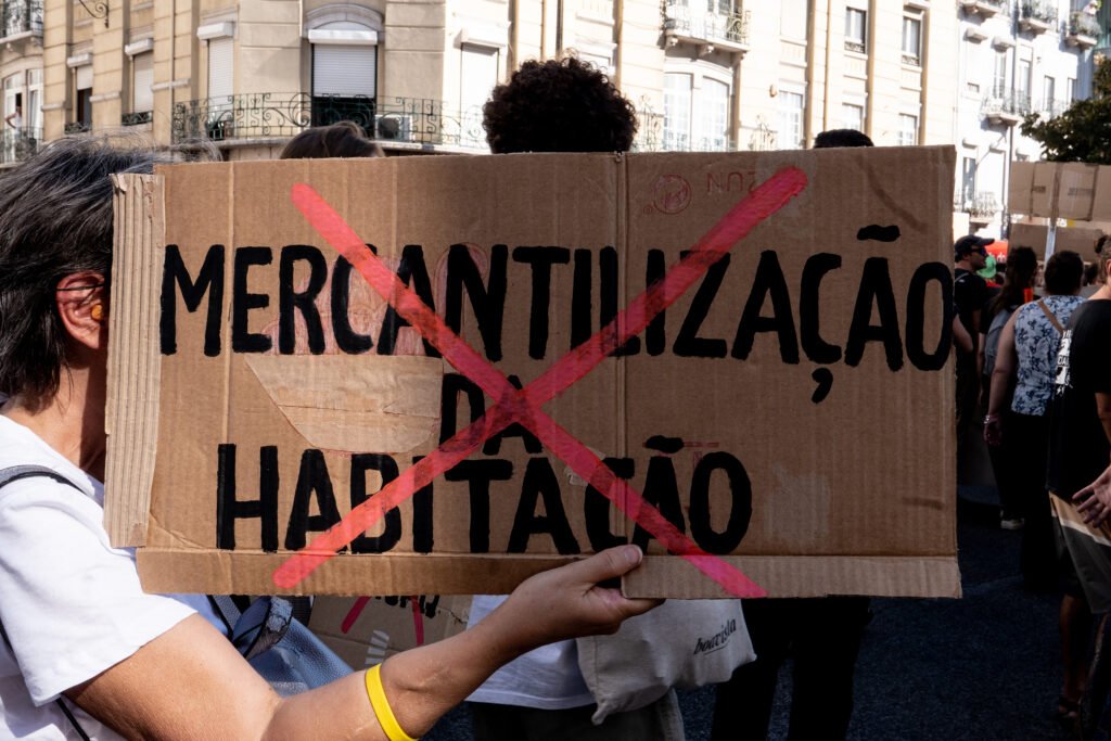 A protester holding a sign with "commercialization of housing" crossed over in Lisbon, Portugal.