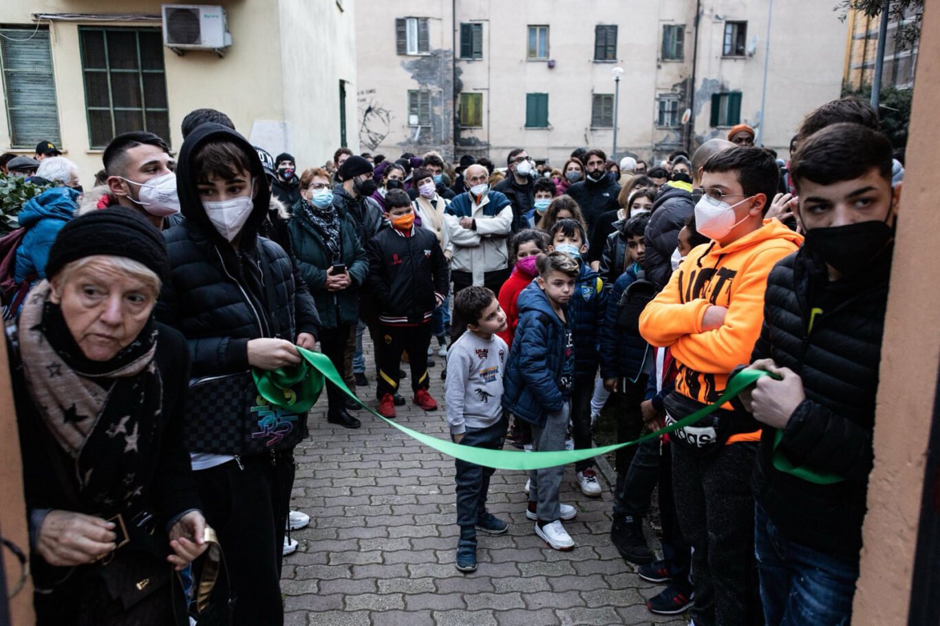 Children are holding a ribbon in front of a crowd, ready to inaugurate new neighborhood center in Quarticciolo, Rome.