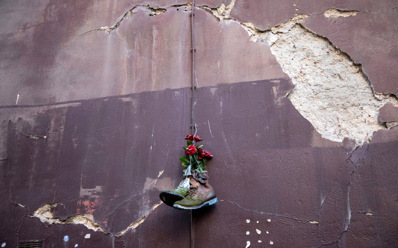 Shoes hanging on a wall with roses inside them.