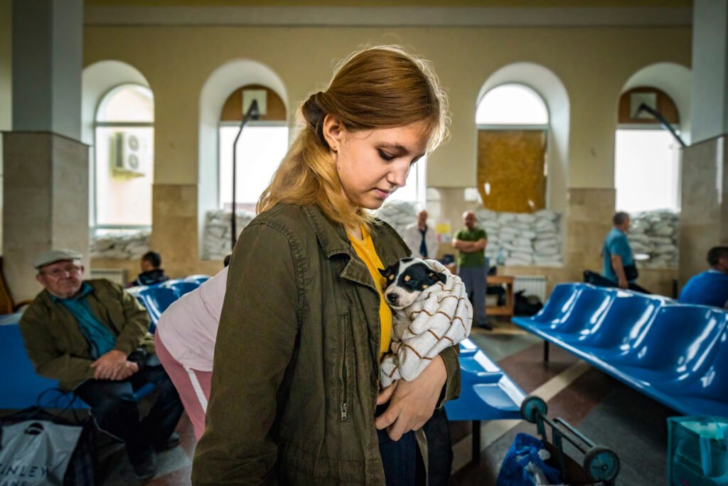 An Ukrainian woman in Kherson with a dog on her arms in train station whose windows are entrenched with sand bags.