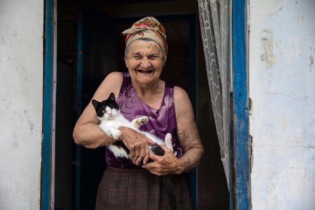 An old Ukrainian woman in Donetsk region stands on her door with a cat on her arms.