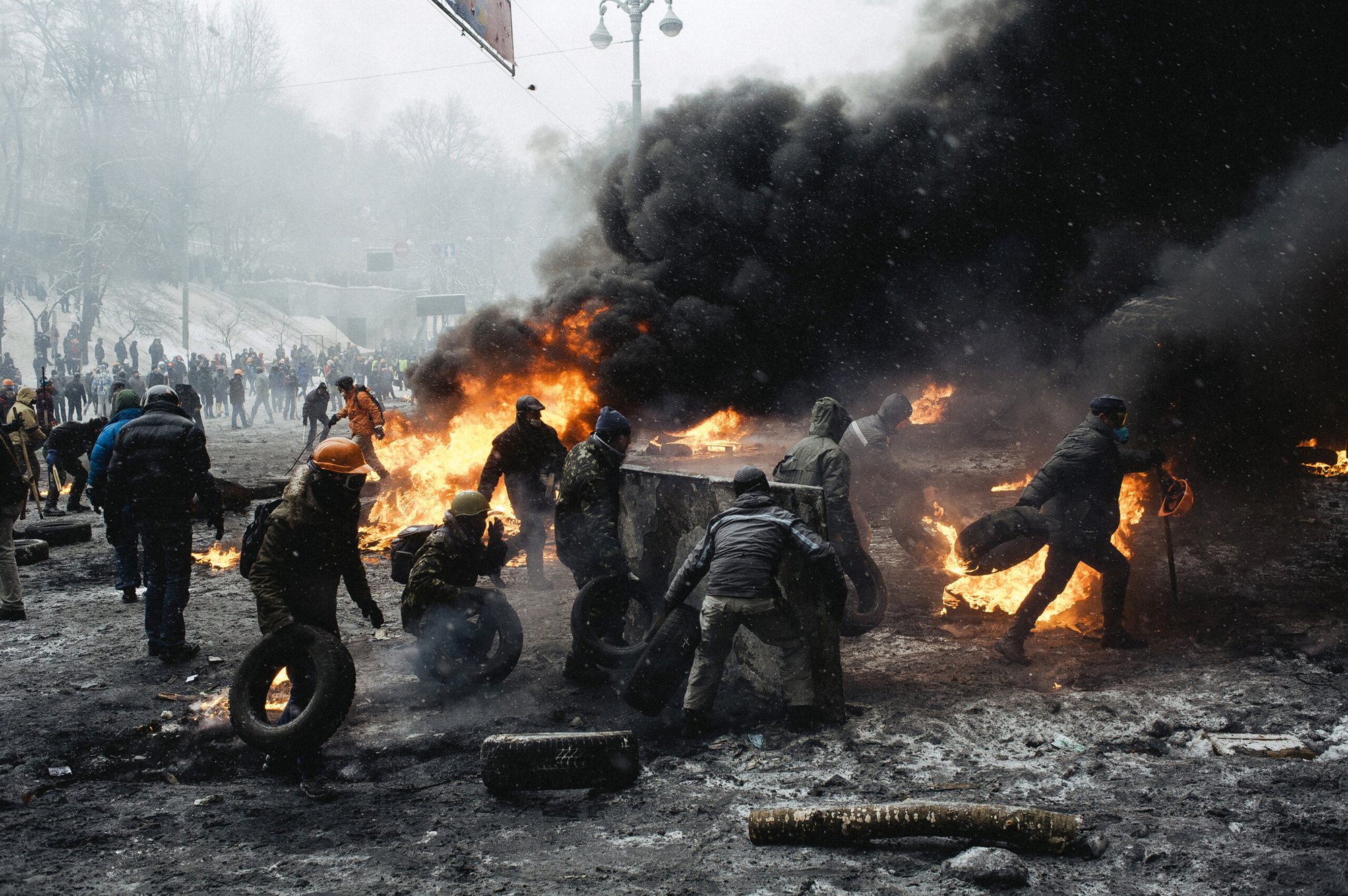 Protesters carry burning car tires closer to the riot police cordon in the center of Kyiv amid black smoke in the Euromaidan protest on January 22, 2014.