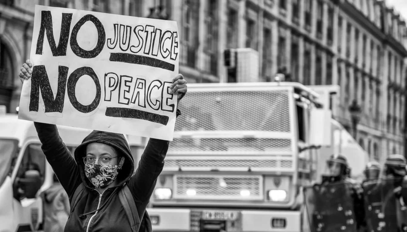 A protester raises a sign reading 'No Justice, No Peace' in front of police vehicles during a Black Lives Matter demonstration in Paris. Moments later, the police moved in on the crowd, making arrests and attempting to disperse them.