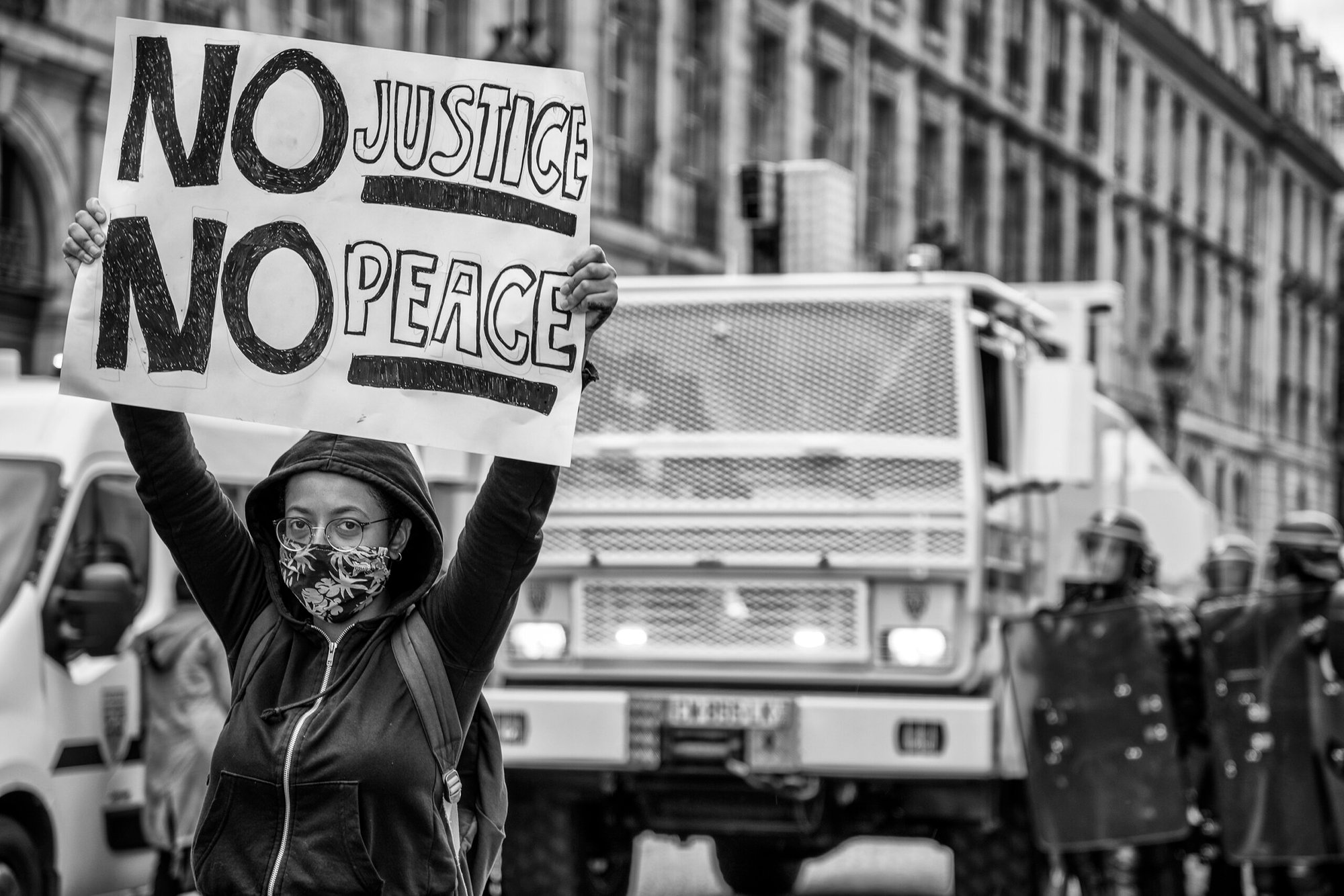 A protester raises a sign reading 'No Justice, No Peace' in front of police vehicles during a Black Lives Matter demonstration in Paris. Moments later, the police moved in on the crowd, making arrests and attempting to disperse them.