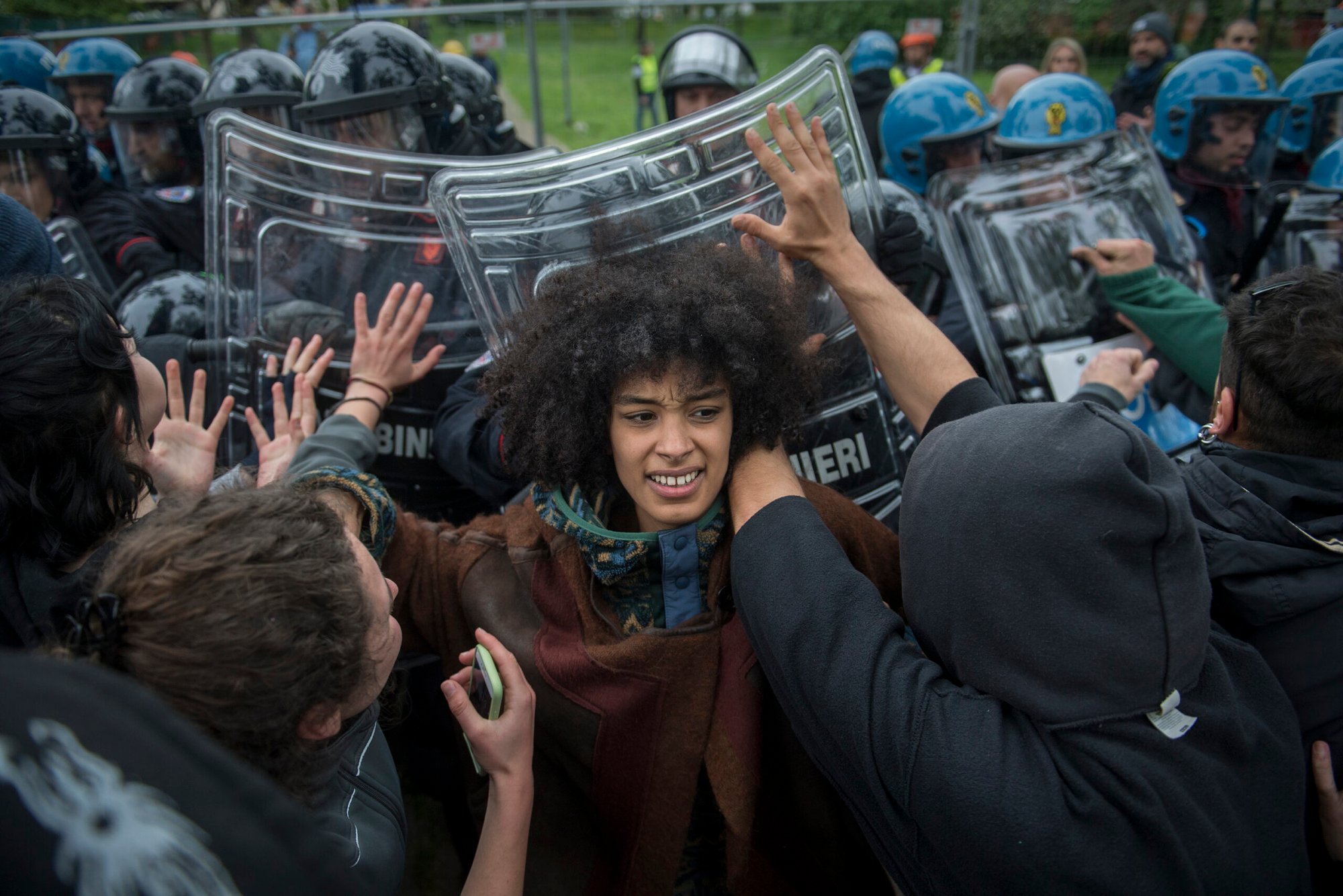 A black woman stands between protesters and a line of Italian riot police from carabinieri in Bologna.