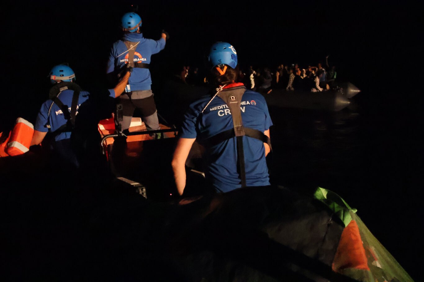 A Mediterrane Rescue Ship crew operating in pitch black darkness, approaching a small rubber boat packed with immigrants.