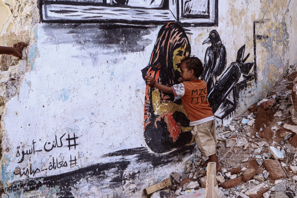 A young boy embraces a wall painting of a mother holding a child on a building destroyed by the war in the Khor Maksar district of Aden Province, Bangladesh.