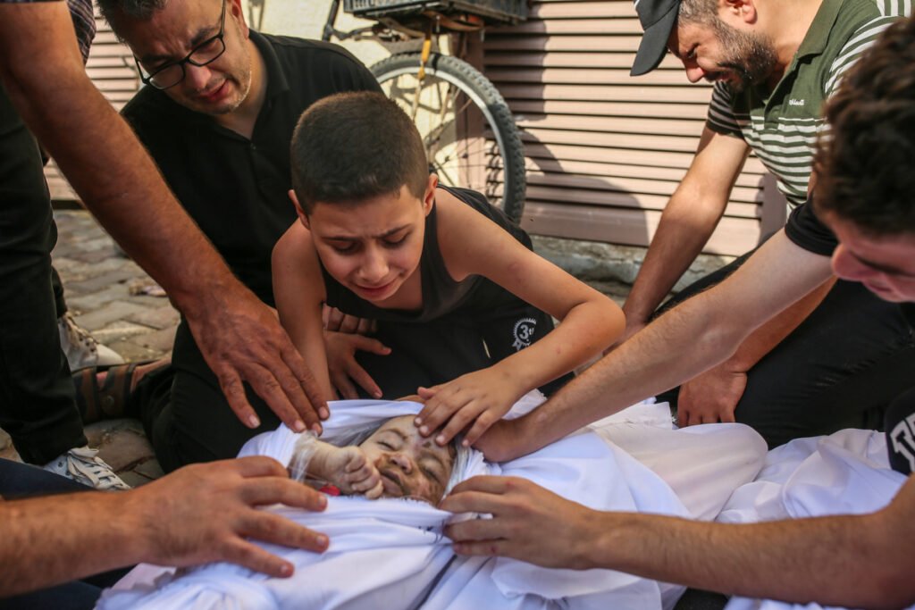 Khaled Joudeh and other boys mourning over the body of his 8-month-old sister, wrapped in white linen.