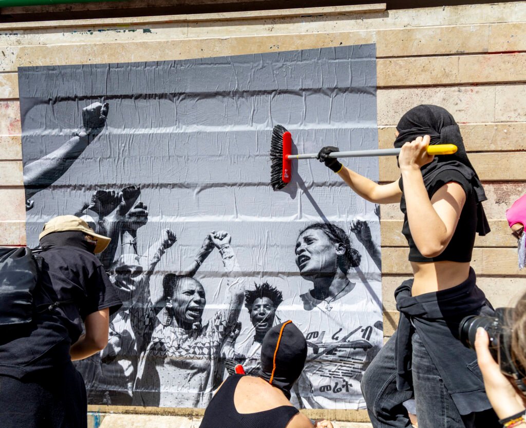 Demonstrators putting up a poster dedicated to Eritrean women during the march, highlighting their struggle and resilience. The poster features Cinzia Canneri's photo of Tigrayan female soldiers alongside Eritrean women.