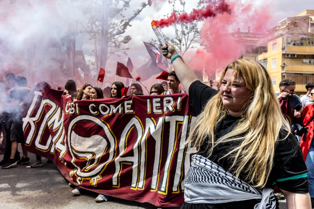 A protester holds a smoke flare at the front of the march as it moves down Via Federico Delpino