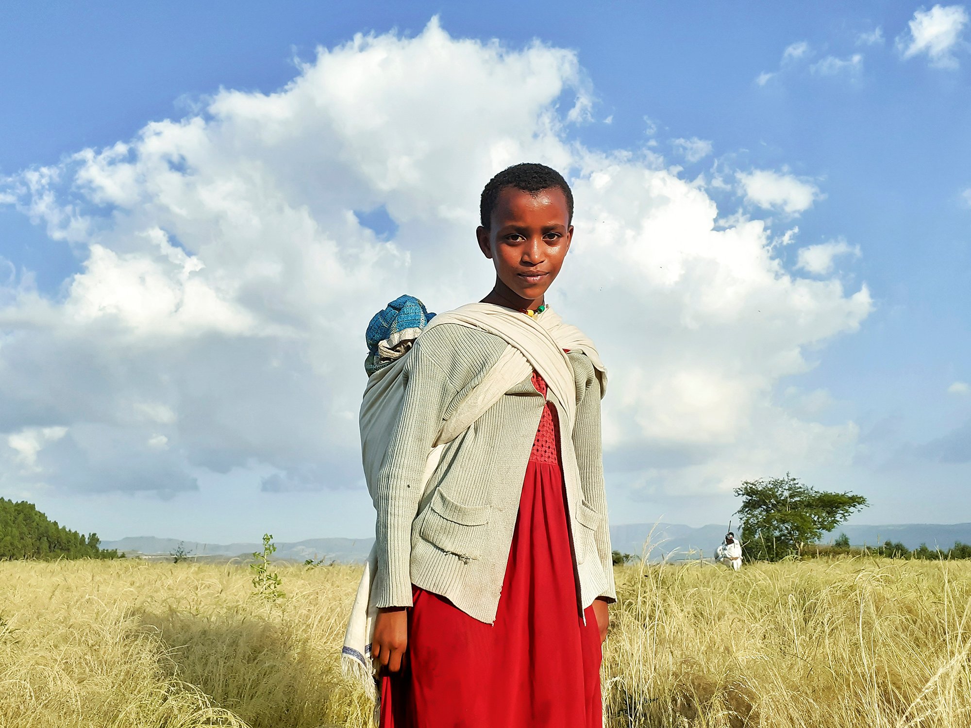 Returning from the market, a young woman stands still for a moment, framed by the quiet beauty of the countryside in Gondar.
